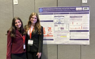Two women in professional dress next to a research poster.